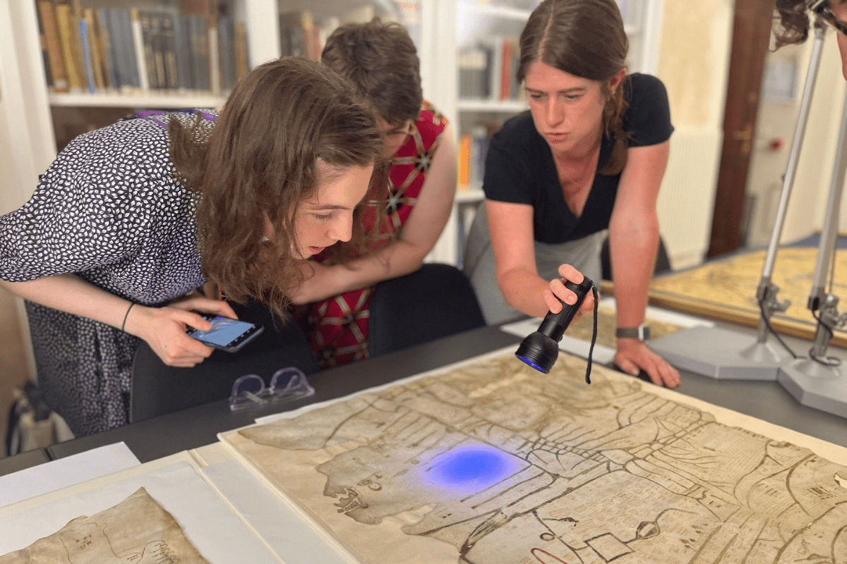Helen Davies with students looking at the Vercelli Mappa Mundi with a UV flashlight in the Vercelli Chapter Library 